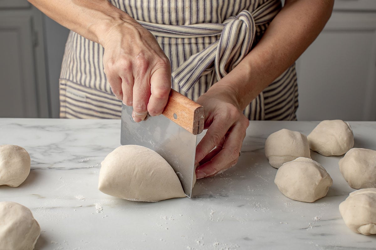 A woman dividing breadstick dough into equal portions.
