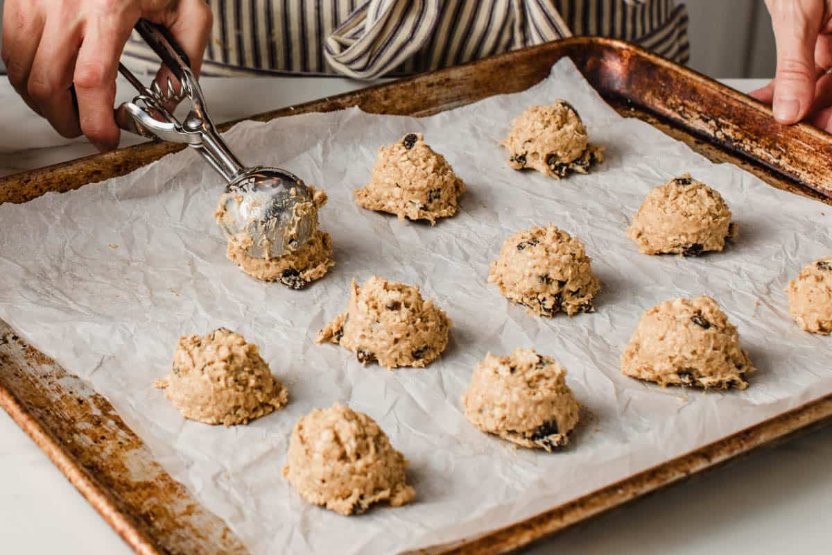 A woman portioning sourdough oatmeal raisin cookie dough with a cookie scoop.
