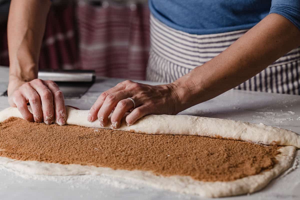A woman rolling up cinnamon roll dough.