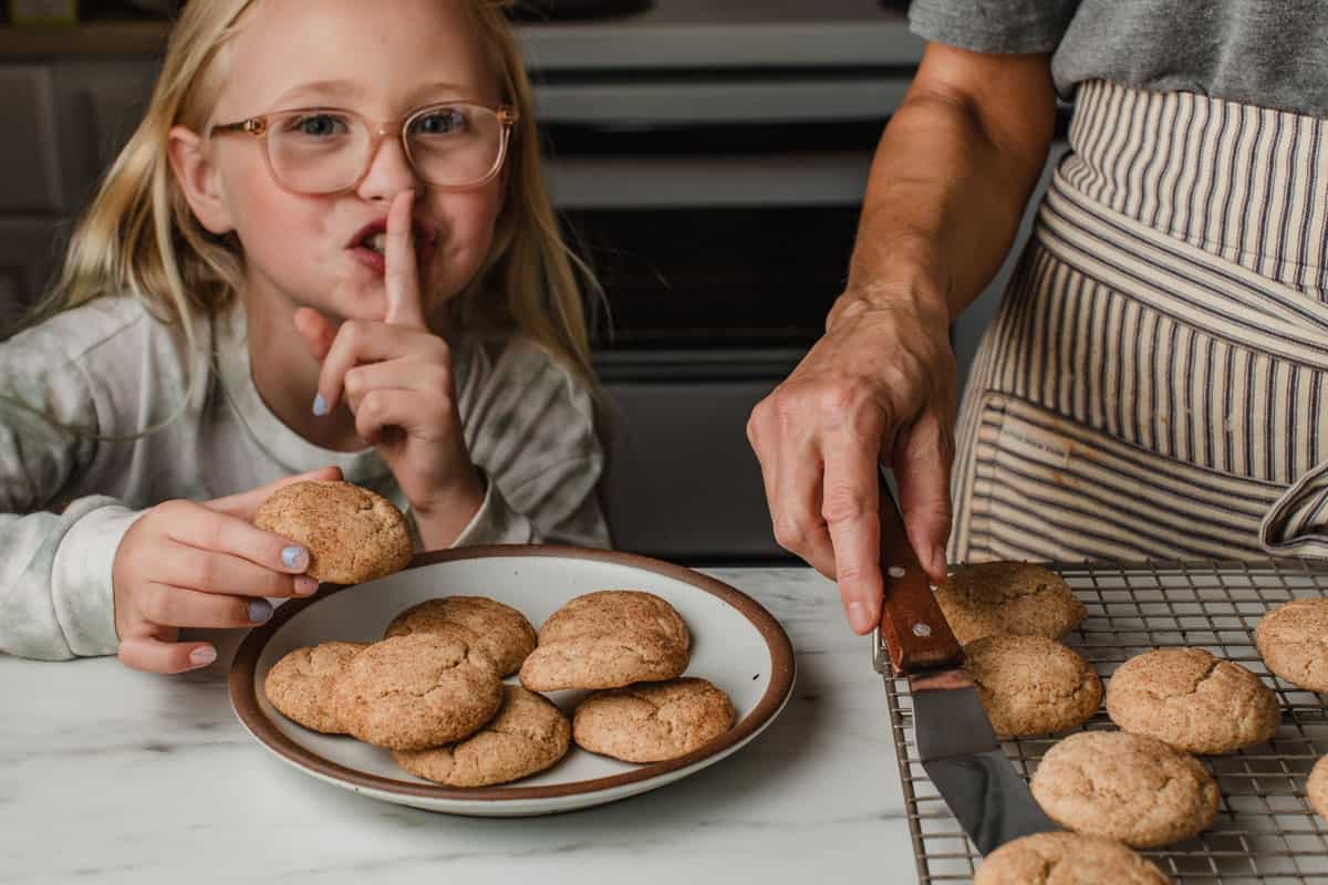 A little girl sneaking a sourdough snickerdoodle cookie from a plate.