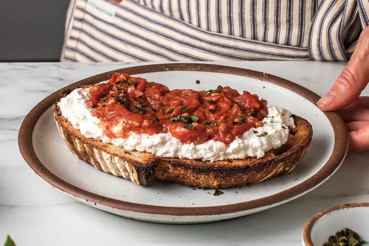 A closeup photo of cherry tomato ricotta toast on a plate.