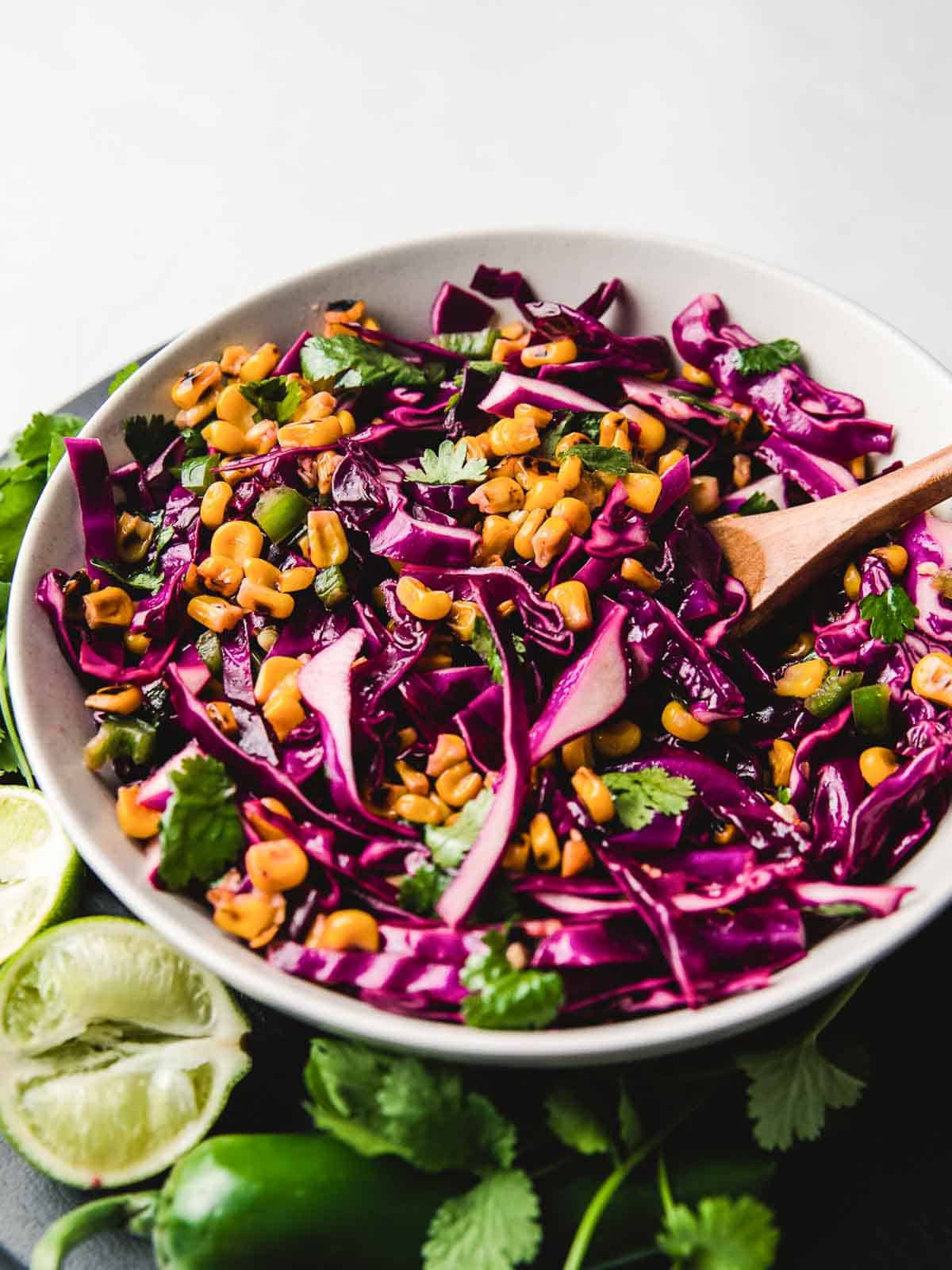 Corn and Red Cabbage Slaw in a bowl with a wooden spoon.