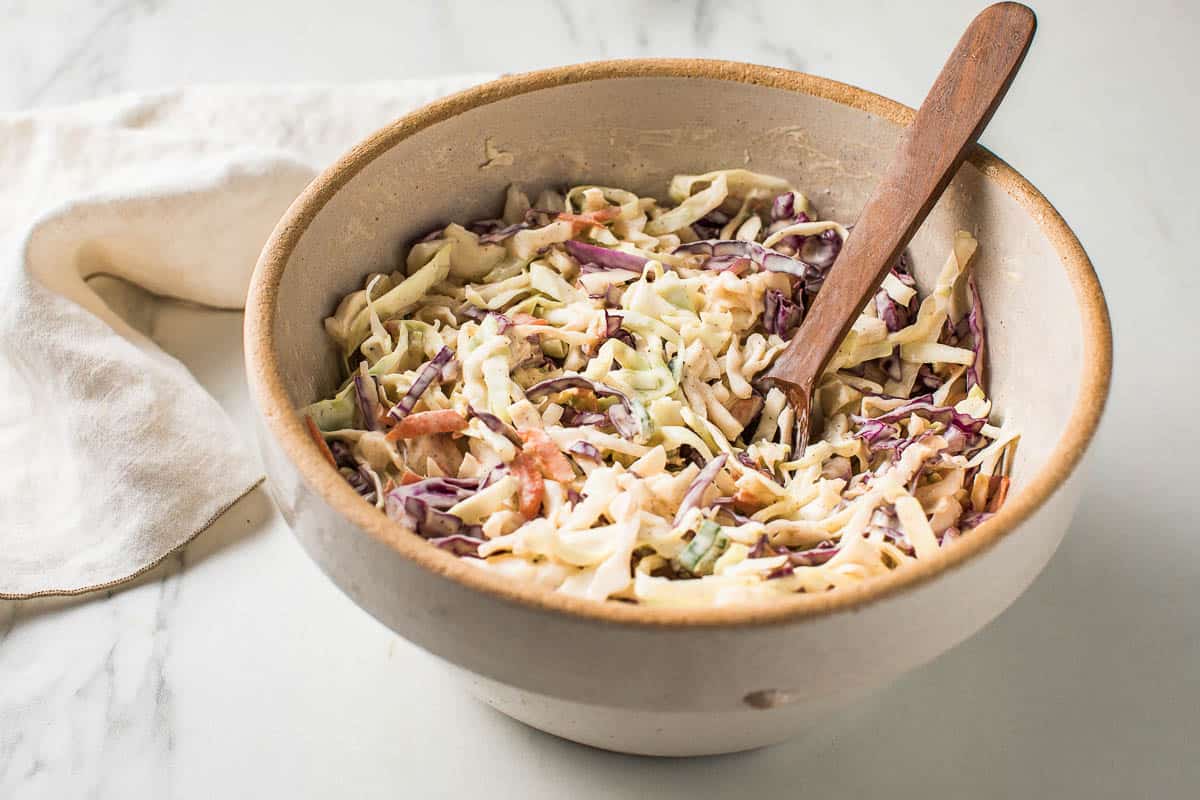 Creamy coleslaw in a serving bowl with a wooden spoon.