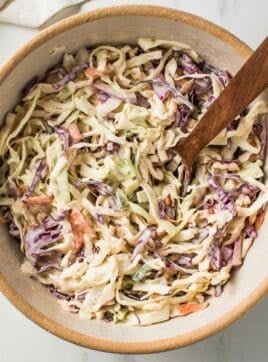 Creamy coleslaw in a bowl with a wooden spoon.