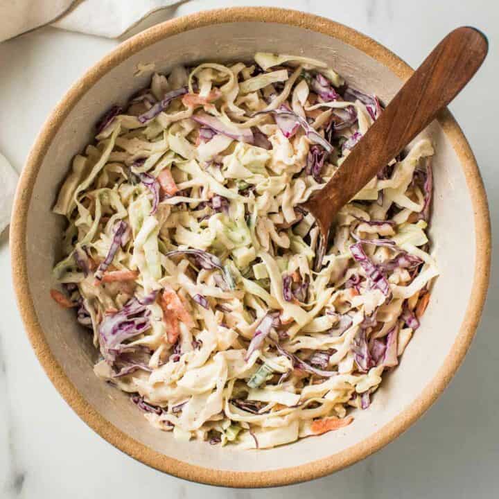 Creamy coleslaw in a bowl with a wooden spoon.
