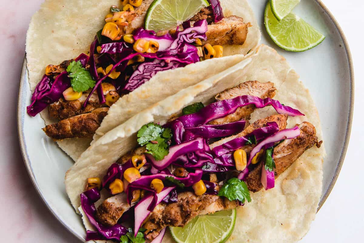 Two chicken tacos on a plate with lime.