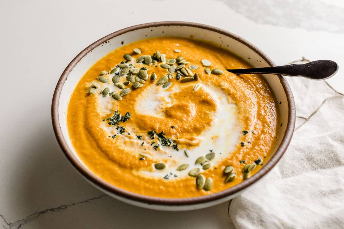 Bowl of pumpkin soup on a table with a spoon.