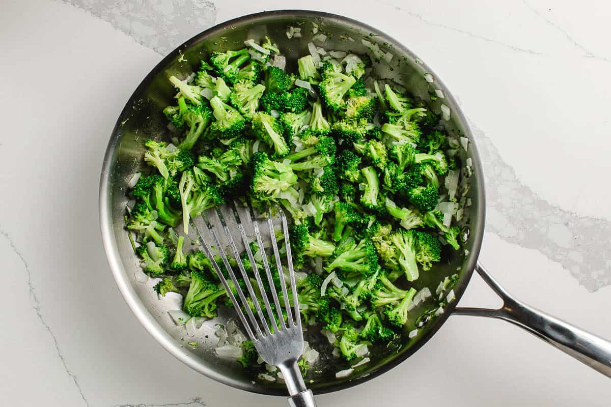 Broccoli and onions sauteing in a pan.