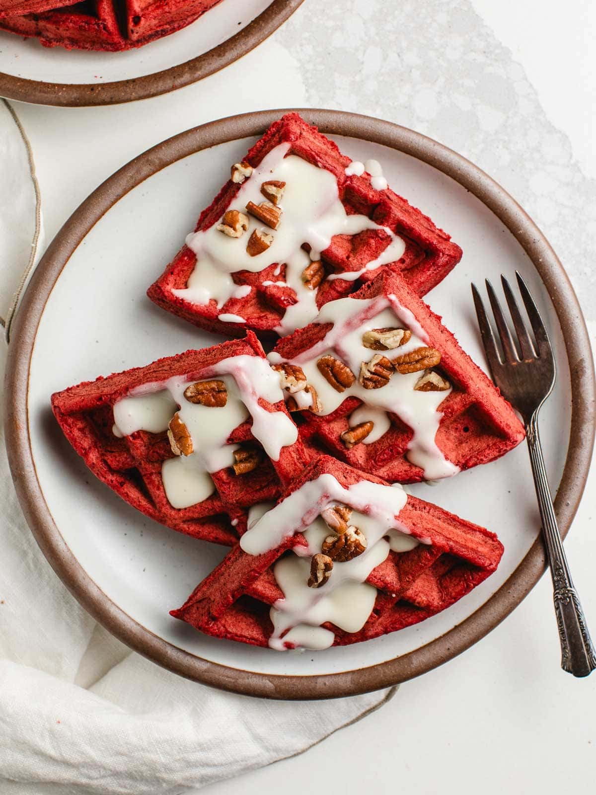 sourdough red velvet waffles on a plate with cream cheese glaze drizzled on top.