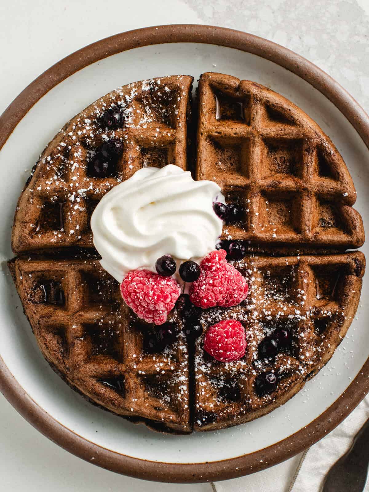 Chocolate sourdough waffles on a plate with berries and whipped cream.