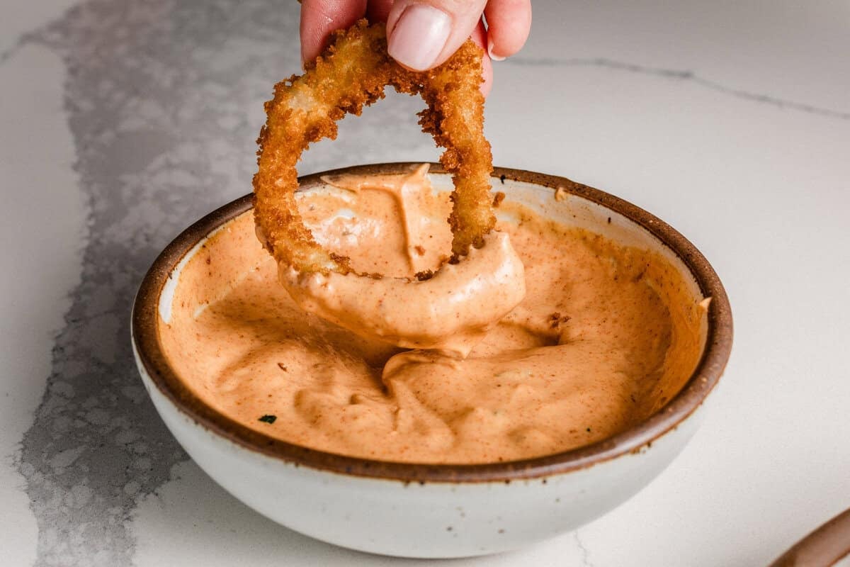A woman dipping a sourdough onion ring in sauce.