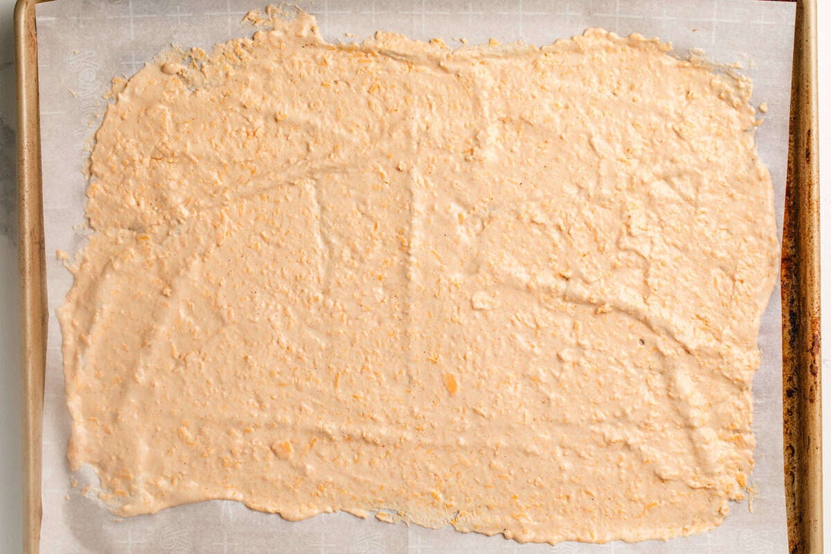 Sourdough cheeze its batter spread out on a parchment paper lined baking sheet.