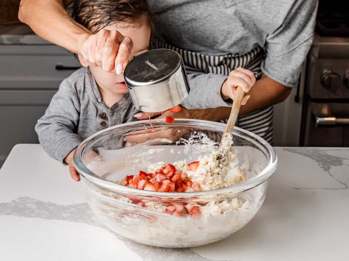 A woman adding fresh chopped strawberries to a bowl of biscuit dough.