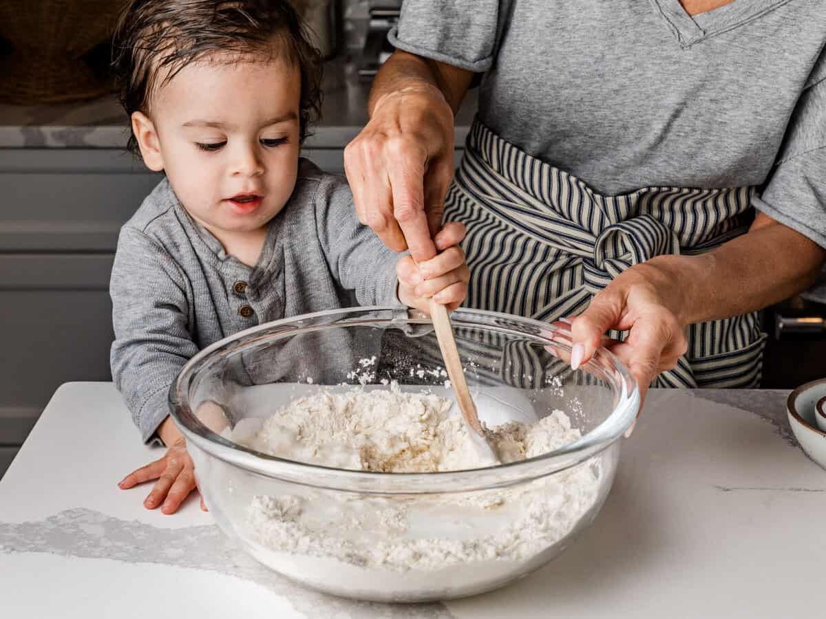 A woman and child mixing the ingredients for sourdough strawberry biscuits in a bowl.