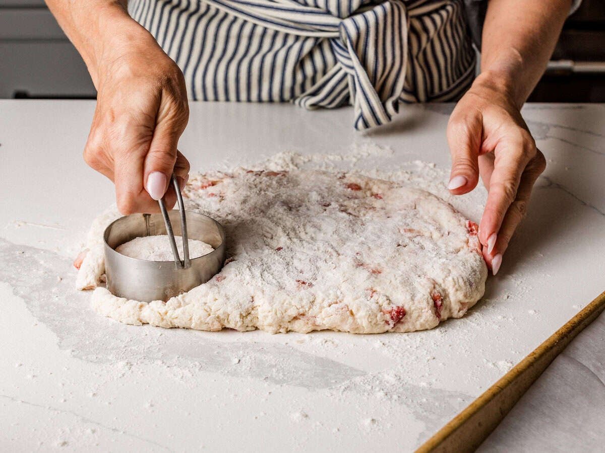A woman cutting out biscuits on a table.