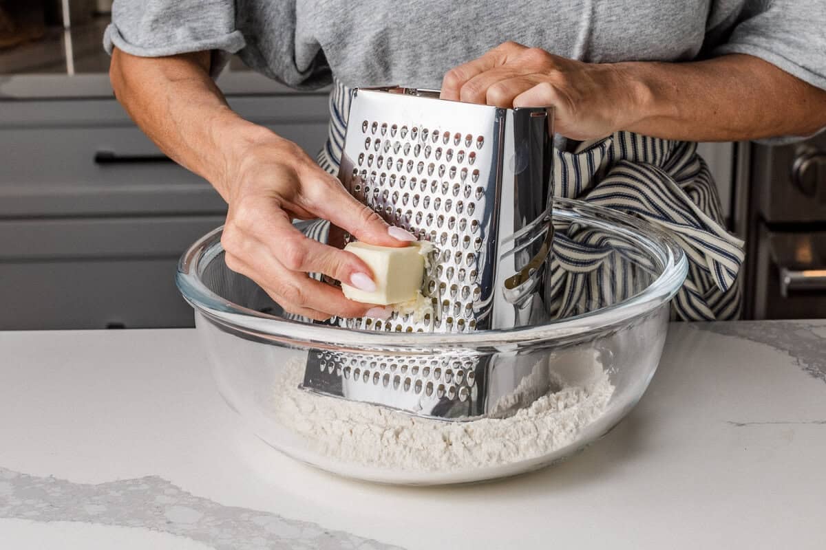 A woman grating butter into a bowl of flour.