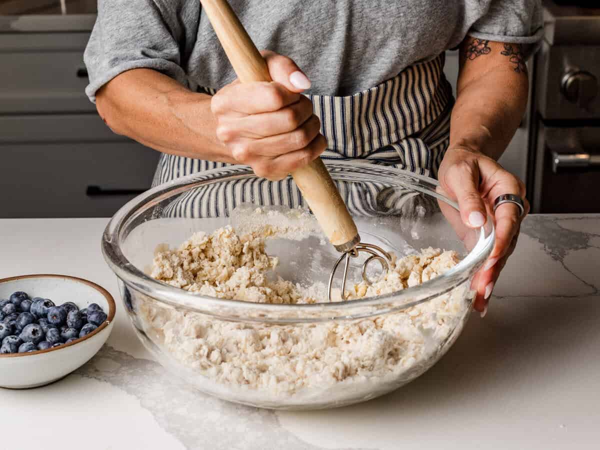 A woman mixing sourdough lemon blueberry scone ingredients in a bowl.