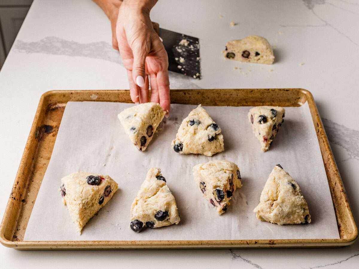 A woman placing sourdough lemon blueberry scone wedges onto a baking sheet.