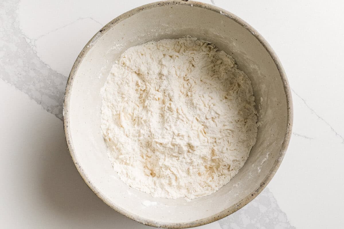Butter grated into a bowl with dry ingredients for sourdough blueberry biscuits.