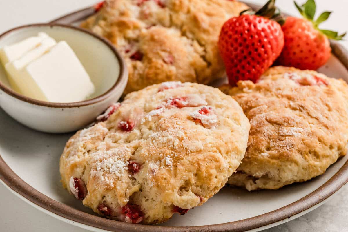 Three sourdough strawberry biscuits on a plate with butter and fresh strawberries.