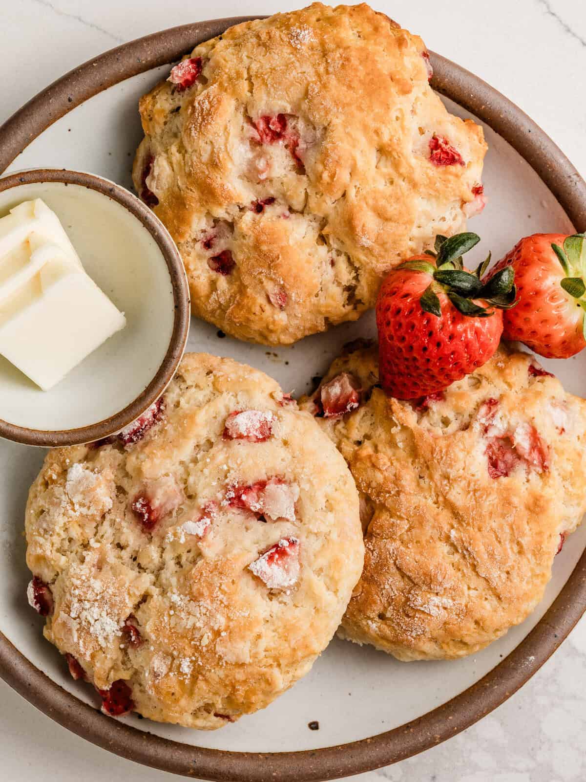 Three sourdough strawberry biscuits on a plate with butter.